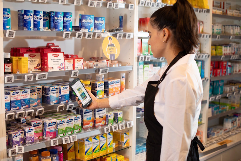 Butikkansatt skanner varer p&aring; apotek med Zebra TC501 og ser produktinformasjon p&aring; skjermen